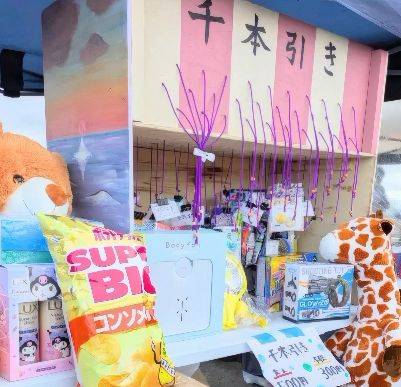 紫のひもが並ぶ千本引きの台と、ぬいぐるみやお菓子の景品