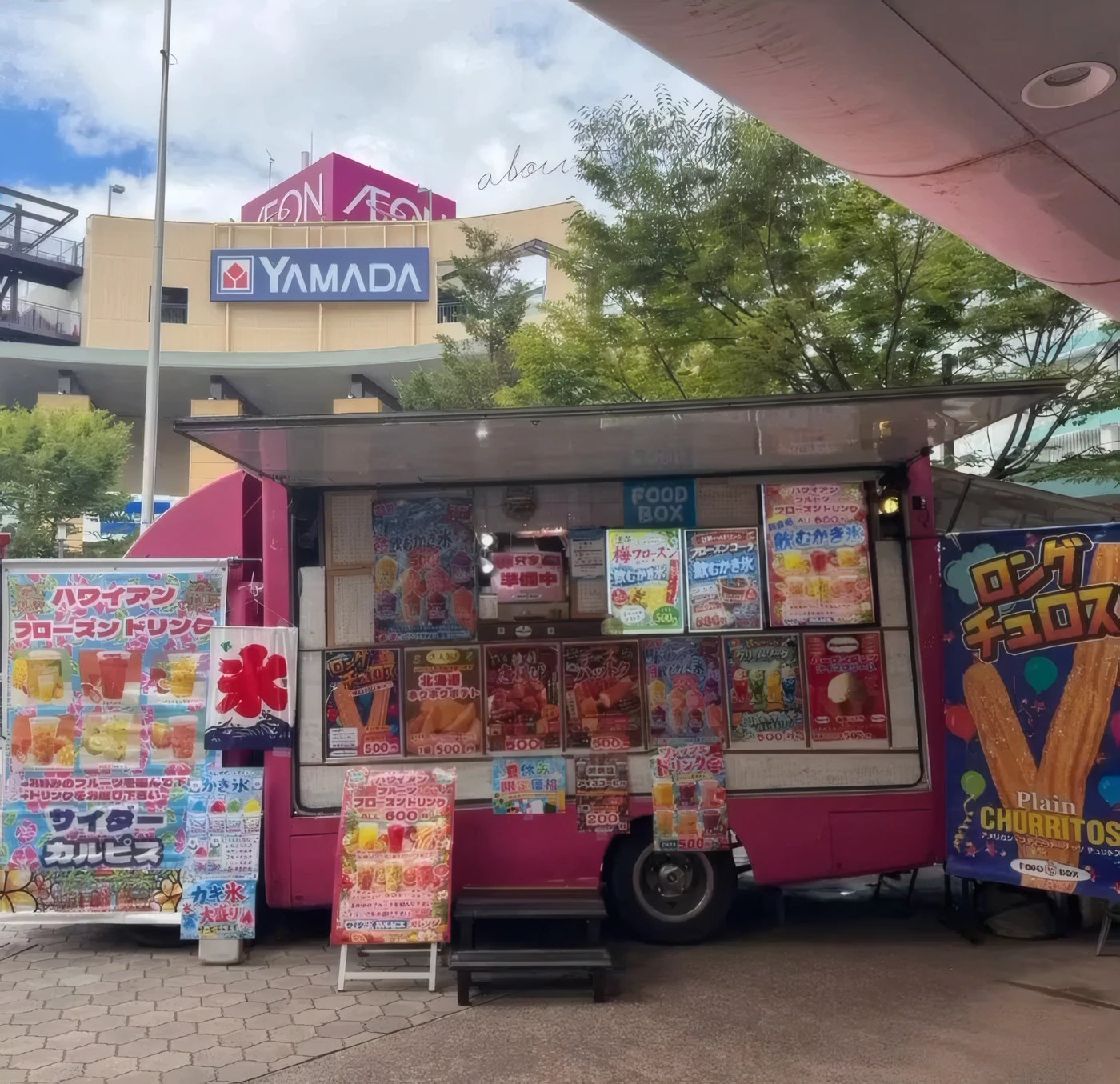 メニューの看板をたくさん掲げたピンクのキッチンカー